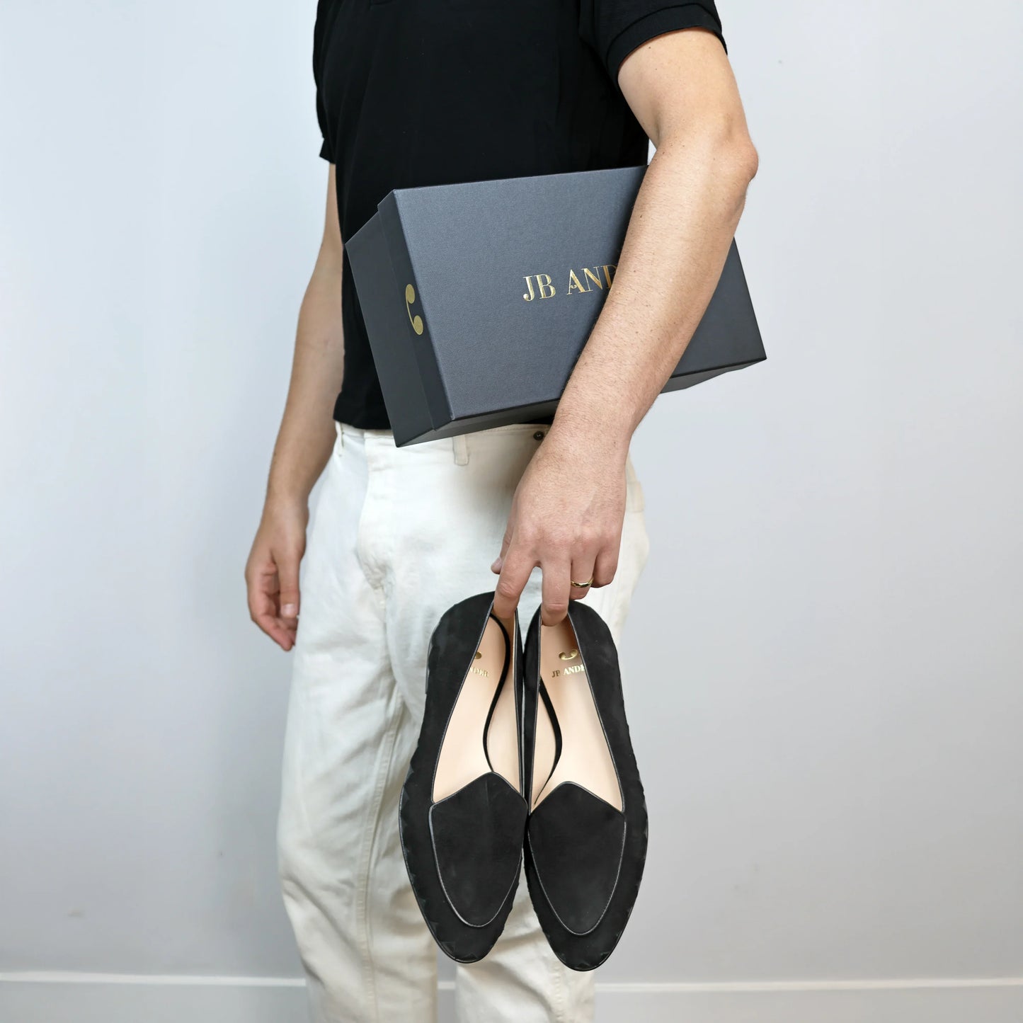 Model holding JB Ander men's Great White smoking slipper loafers in Nero black suede with unique leather trim, and handmade Italian craftsmanship.