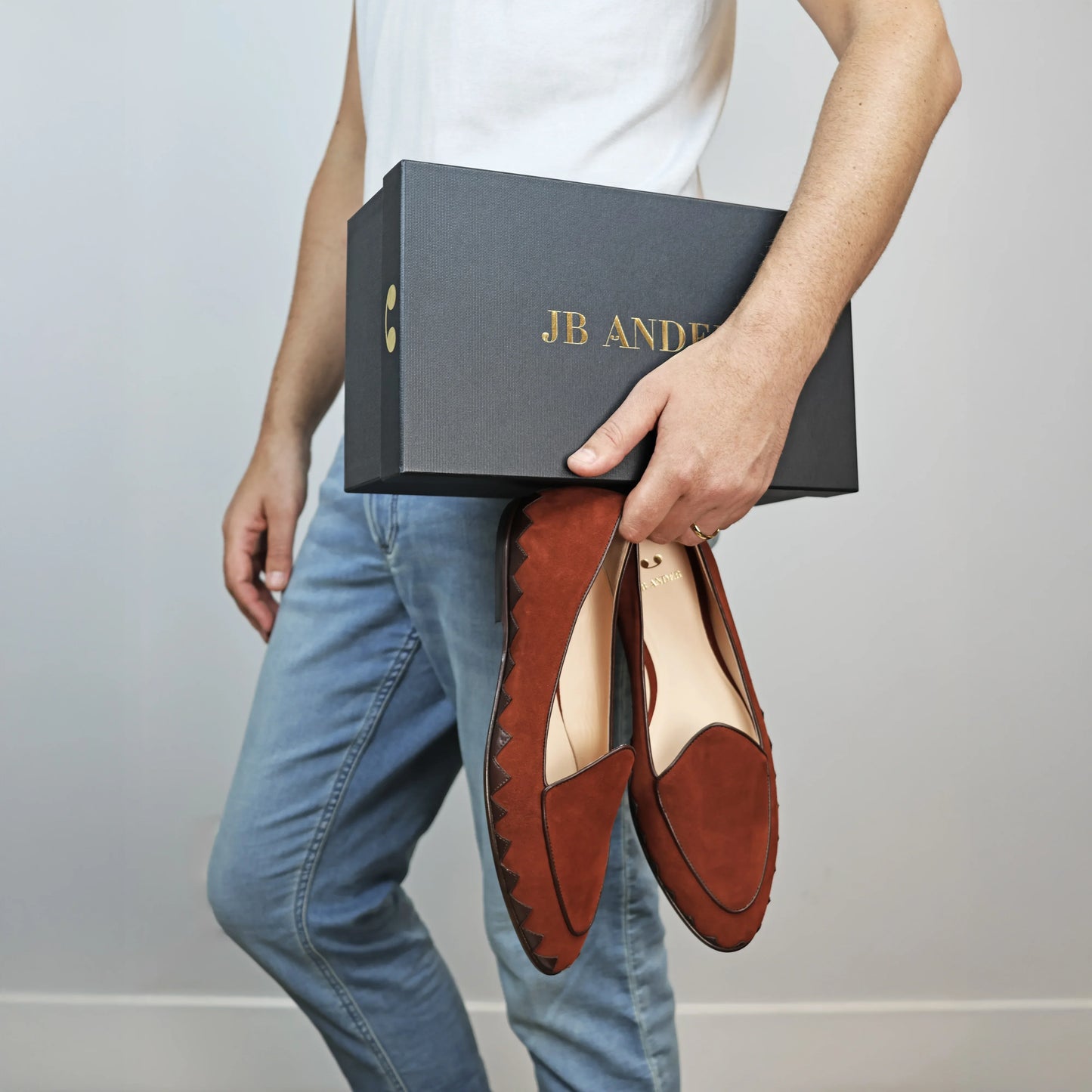 Model holding JB Ander men's Great White smoking slipper loafers in SoHo Sunset burnt umber suede with unique leather trim, and handmade Italian craftsmanship.