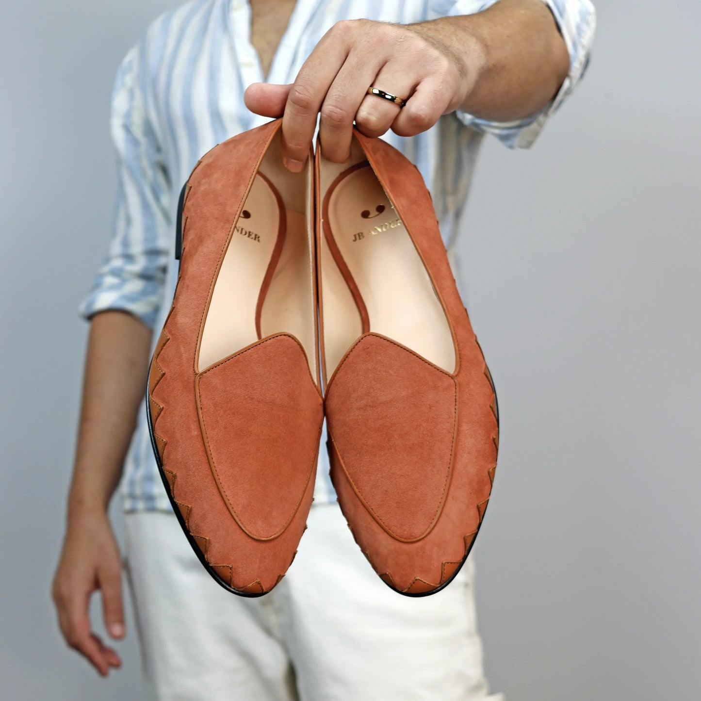 Model holding JB Ander men's Great White smoking slipper loafers in terracotta suede with unique leather trim, and handmade Italian craftsmanship.