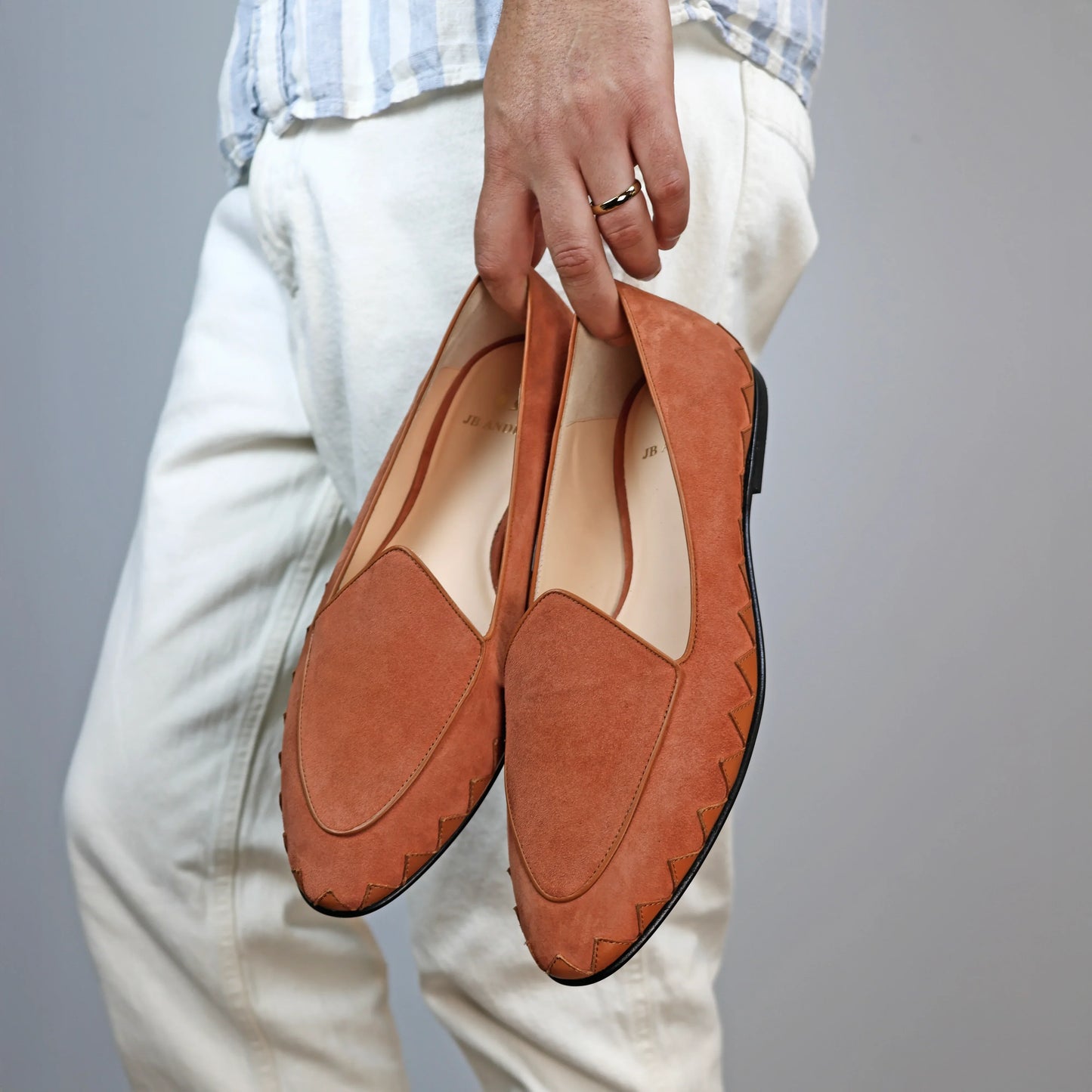 Model holding JB Ander men's Great White smoking slipper loafers in terracotta suede with unique leather trim, and handmade Italian craftsmanship.