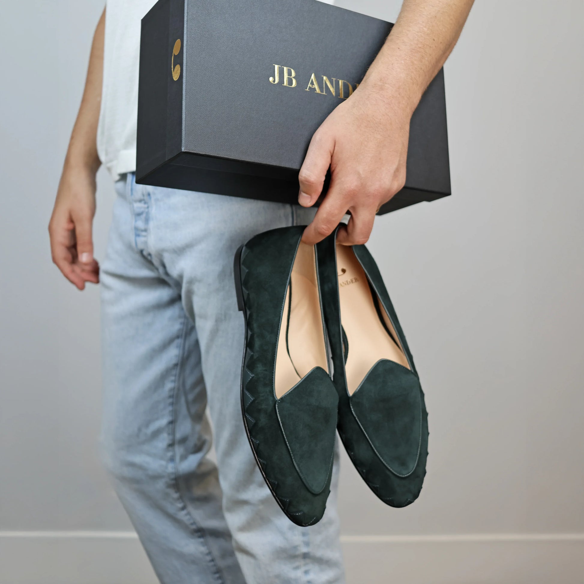 Model holding JB Ander men's Great White smoking slipper loafers in Verde green suede with unique leather trim, and handmade Italian craftsmanship.
