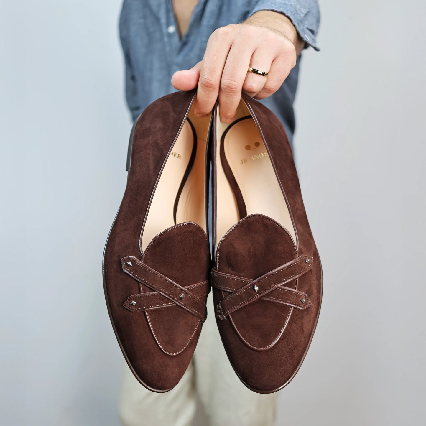 Model holding JB Ander's Lincoln saddle loafer in brown Italian suede – handcrafted in Italy with dual leather straps on vamp, antiqued gold hardware, and luxurious calfskin insole.