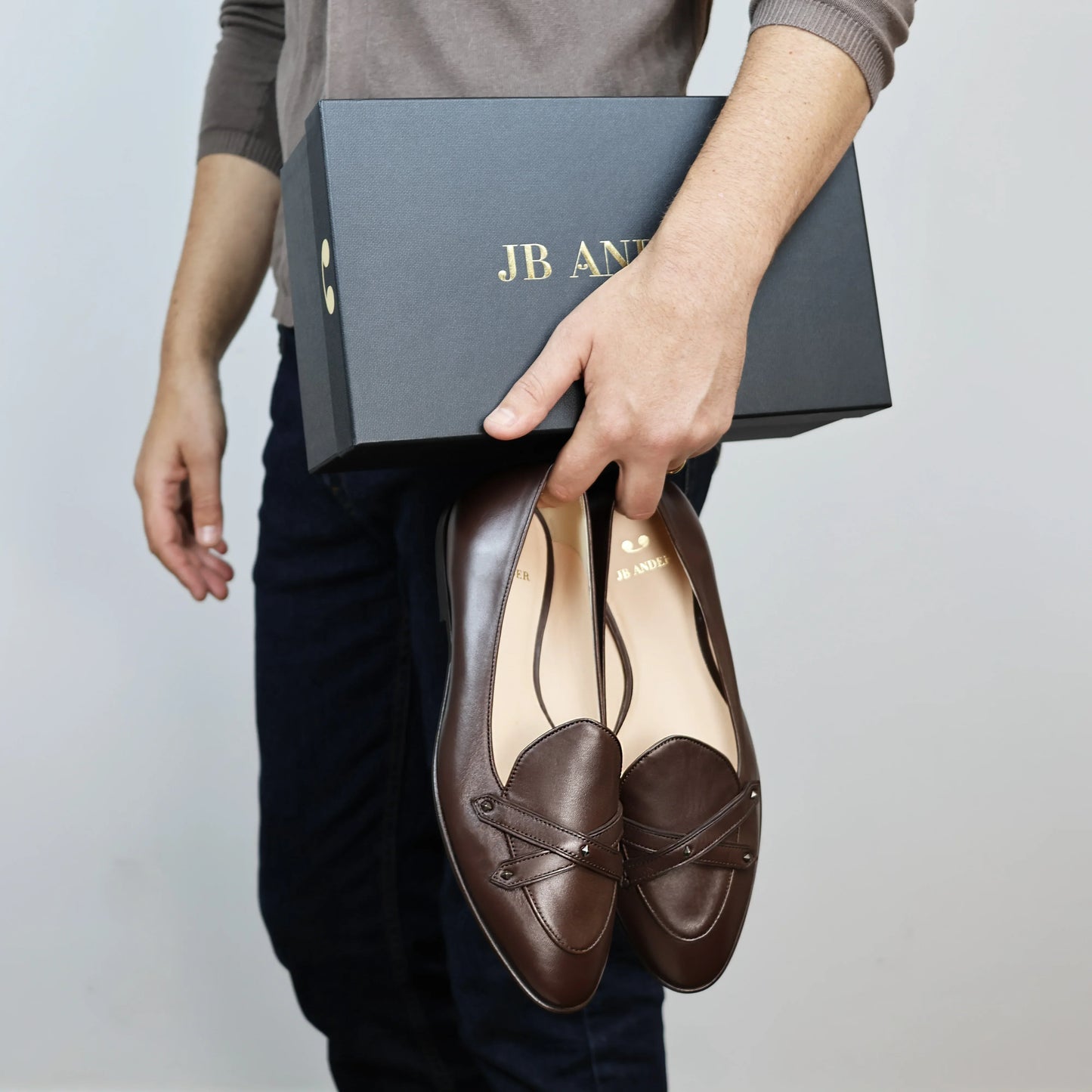 Model holding JB Ander's Lincoln saddle loafer in chestnut brown Italian leather – handcrafted in Italy with dual straps on vamp, antiqued gold hardware, and luxurious calfskin insole.