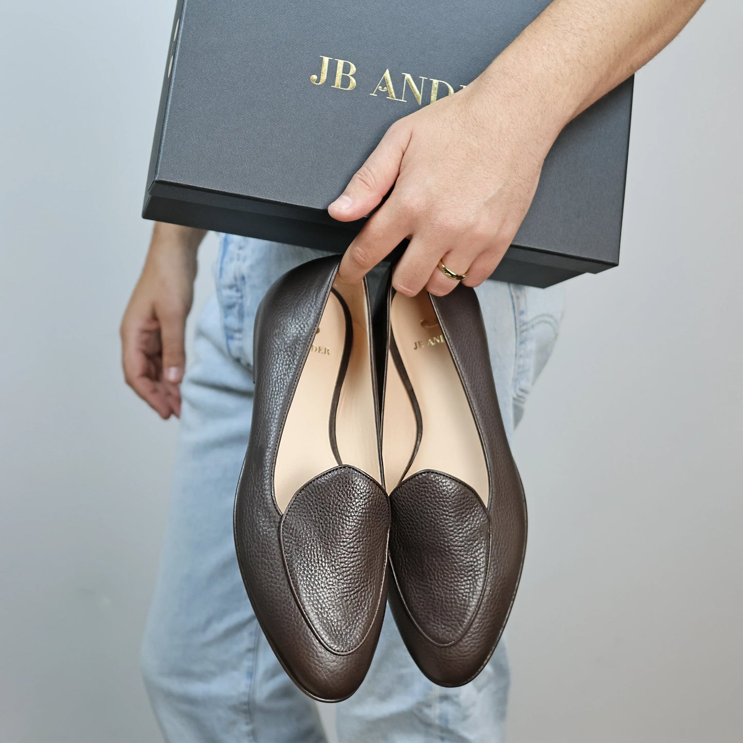 Model holding JB Ander's Venetian loafers in espresso brown pebbled leather, luxurious calfskin insole, and handcrafted in Italy .