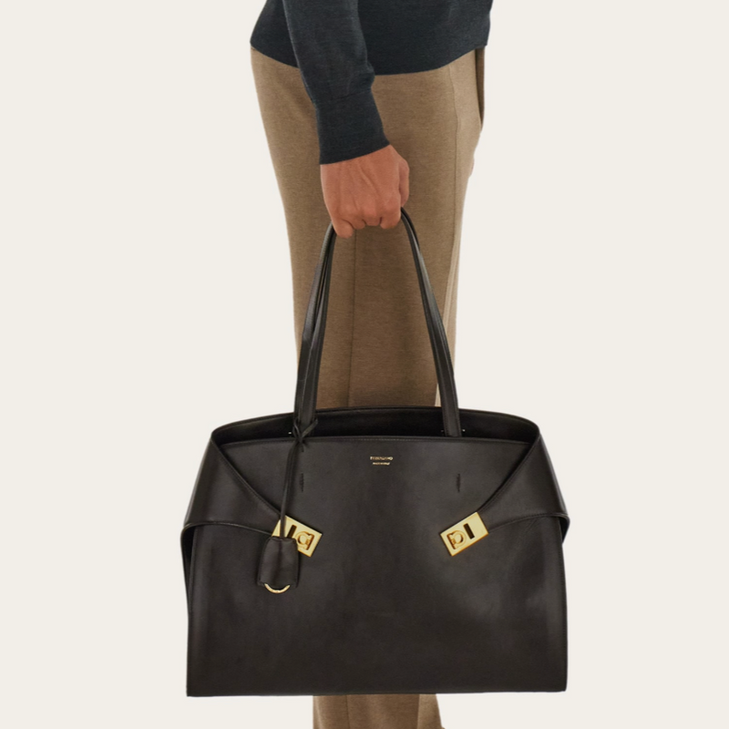 Person holding a Ferragamo hug bag with gold accents on a plain background