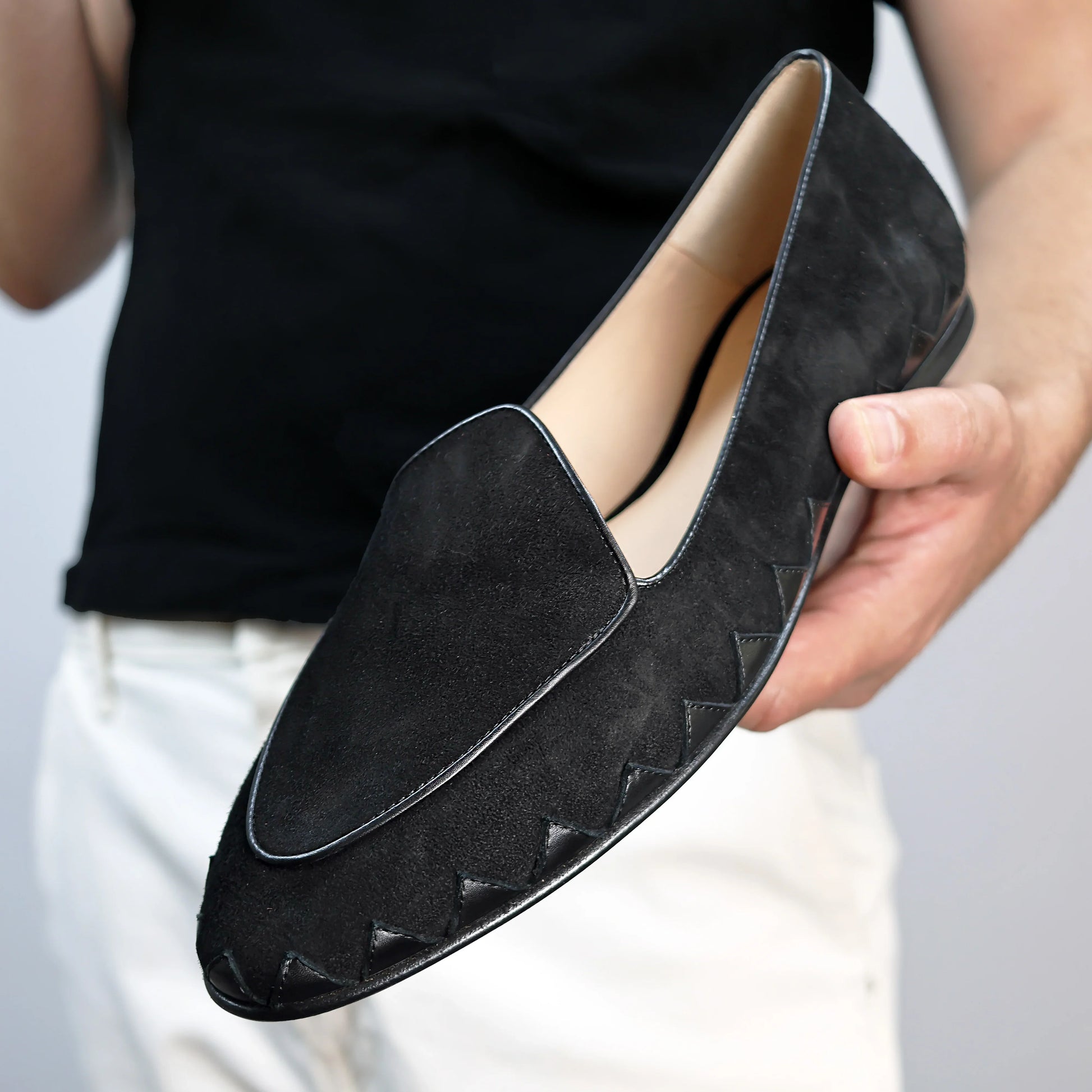 Model holding JB Ander men's Great White smoking slipper loafers in Nero black suede with unique leather trim, and handmade Italian craftsmanship.