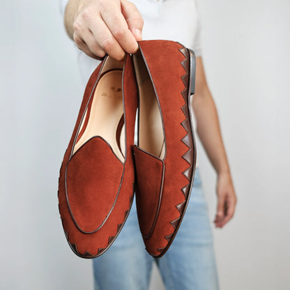Model holding JB Ander men's Great White smoking slipper loafers in SoHo Sunset burnt umber suede with unique leather trim, and handmade Italian craftsmanship.