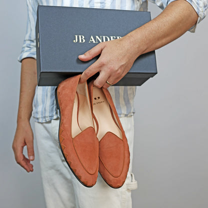 Model holding JB Ander men's Great White smoking slipper loafers in terracotta suede with unique leather trim, and handmade Italian craftsmanship.