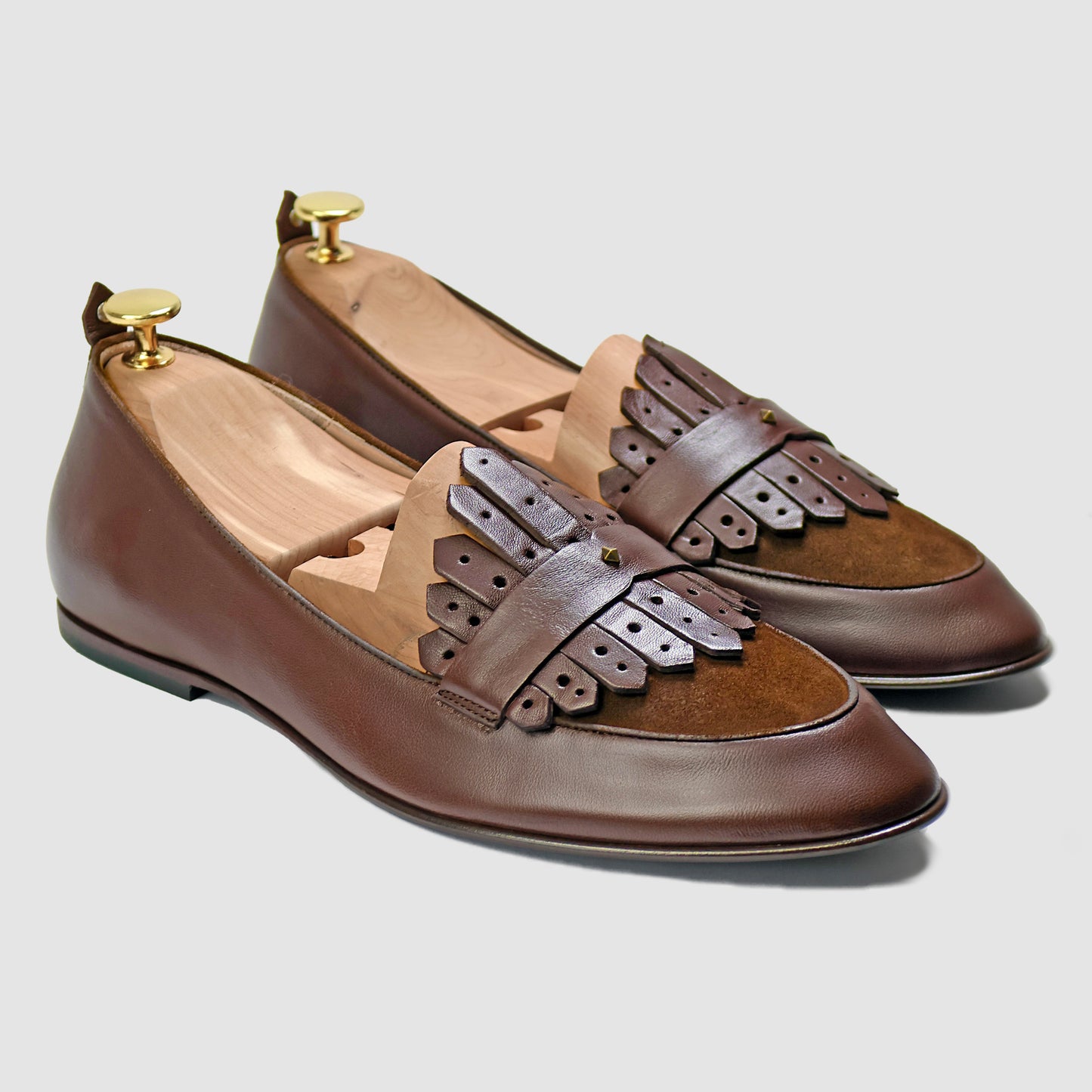 Chestnut brown Italian leather Scottie kilt loafers by JB Ander, front three-quarter angle showing double leather fringe kiltie detail, suede trim, and antiqued gold metal accessories. 