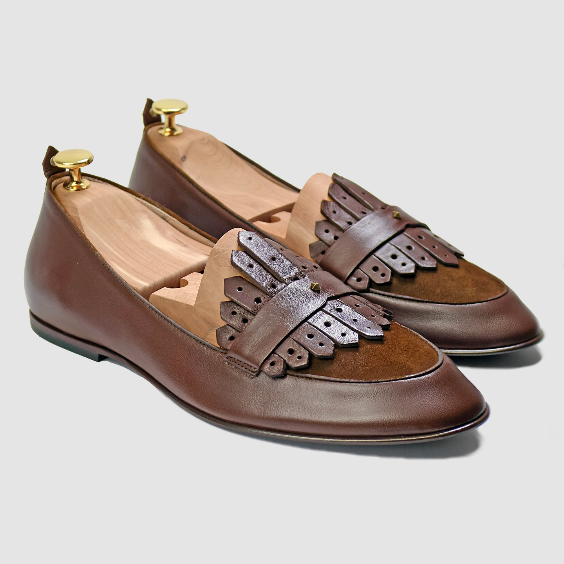 Chestnut brown Italian leather Scottie kilt loafers by JB Ander, front three-quarter angle showing double leather fringe kiltie detail, suede trim, and antiqued gold metal accessories. 