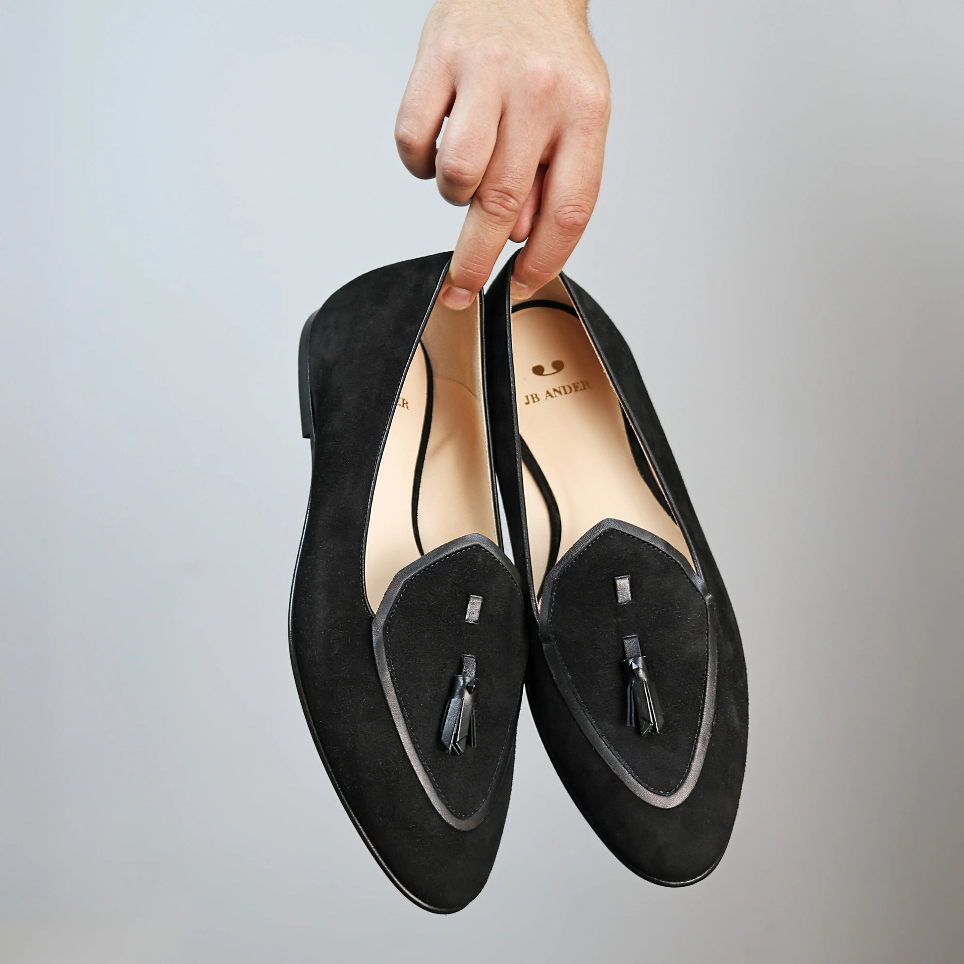 Model holding JB Ander men's Valedictorian tassel loafers in Nero black suede with black leather trim, and handmade Italian craftsmanship.