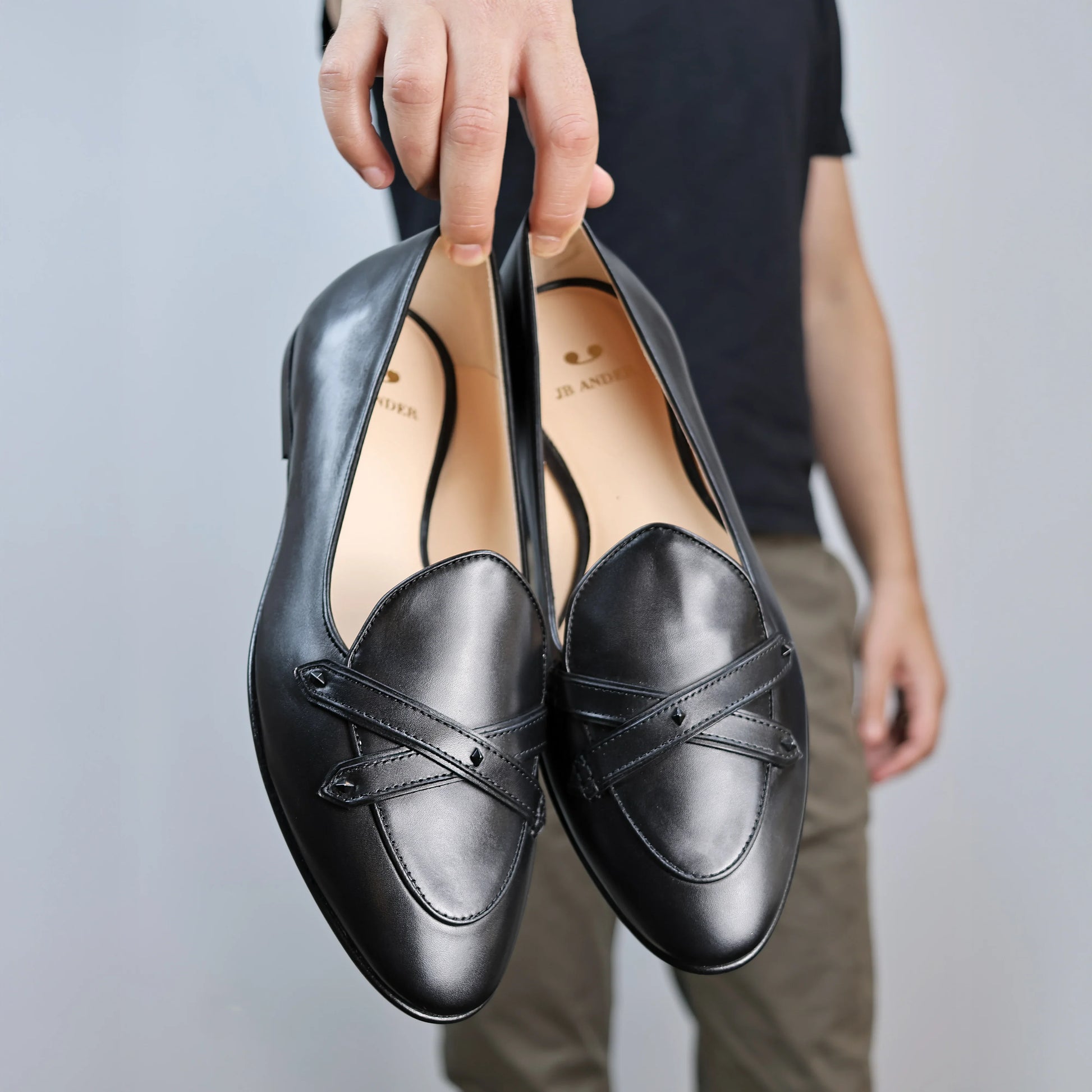 Model holding JB Ander's Lincoln saddle loafer in Nero black Italian leather – handcrafted in Italy with dual straps on vamp, and luxurious calfskin insole.