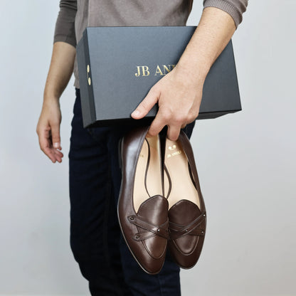 Model holding JB Ander's Lincoln saddle loafer in chestnut brown Italian leather – handcrafted in Italy with dual straps on vamp, antiqued gold hardware, and luxurious calfskin insole.