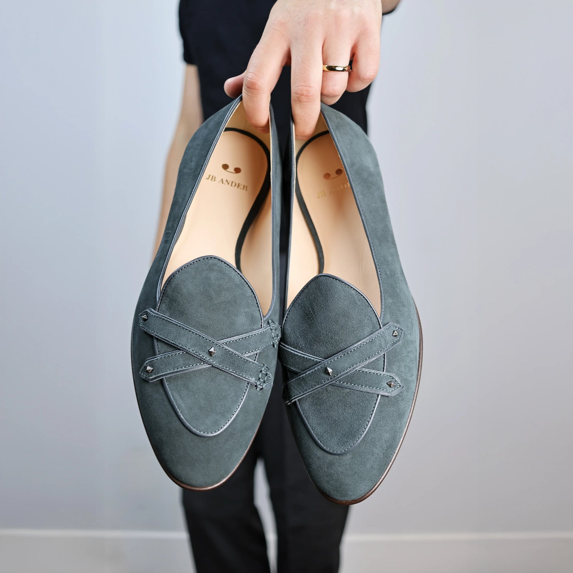 Model holding JB Ander's Lincoln saddle loafer in emerald green Italian suede – handcrafted in Italy with dual leather straps on vamp, antiqued gold hardware, and luxurious calfskin insole.