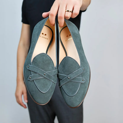 Model holding JB Ander's Lincoln saddle loafer in emerald green Italian suede – handcrafted in Italy with dual leather straps on vamp, antiqued gold hardware, and luxurious calfskin insole.