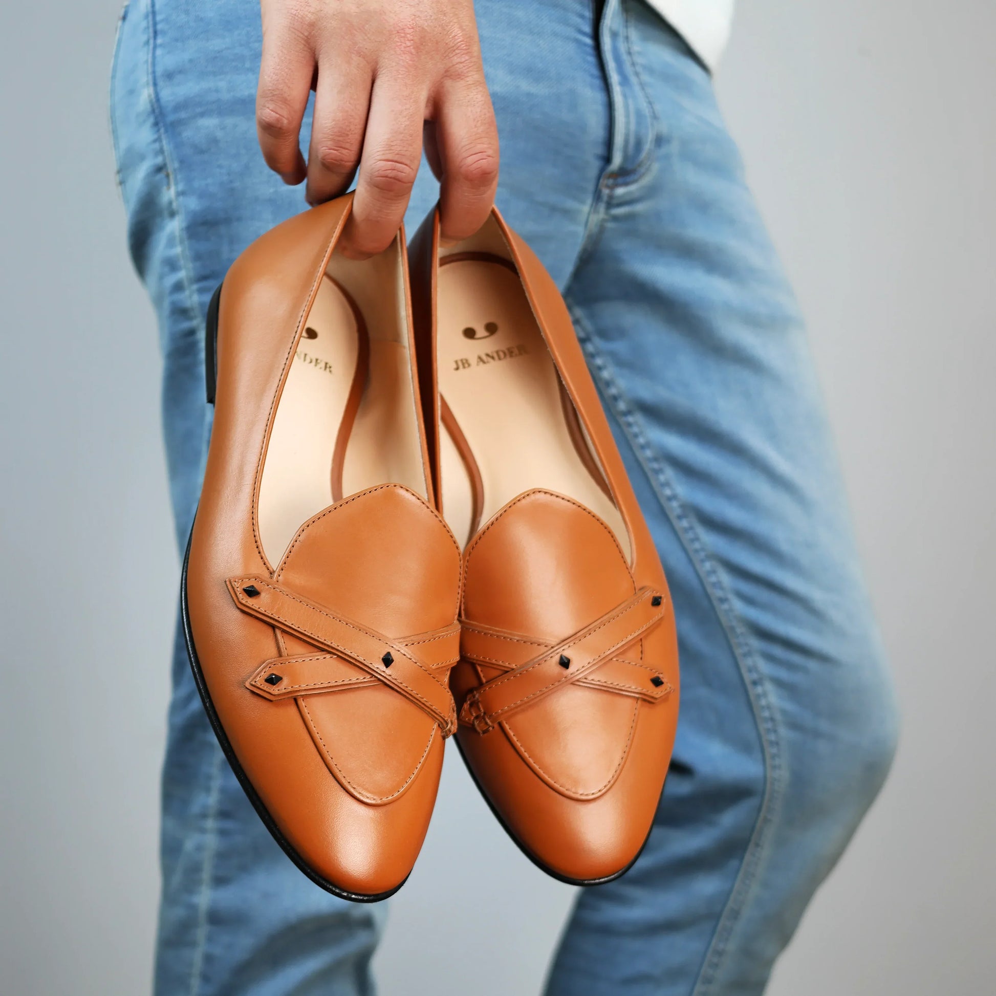 Model holding JB Ander's Lincoln saddle loafer in terracotta Italian leather – handcrafted in Italy with dual straps on vamp, and luxurious calfskin insole.