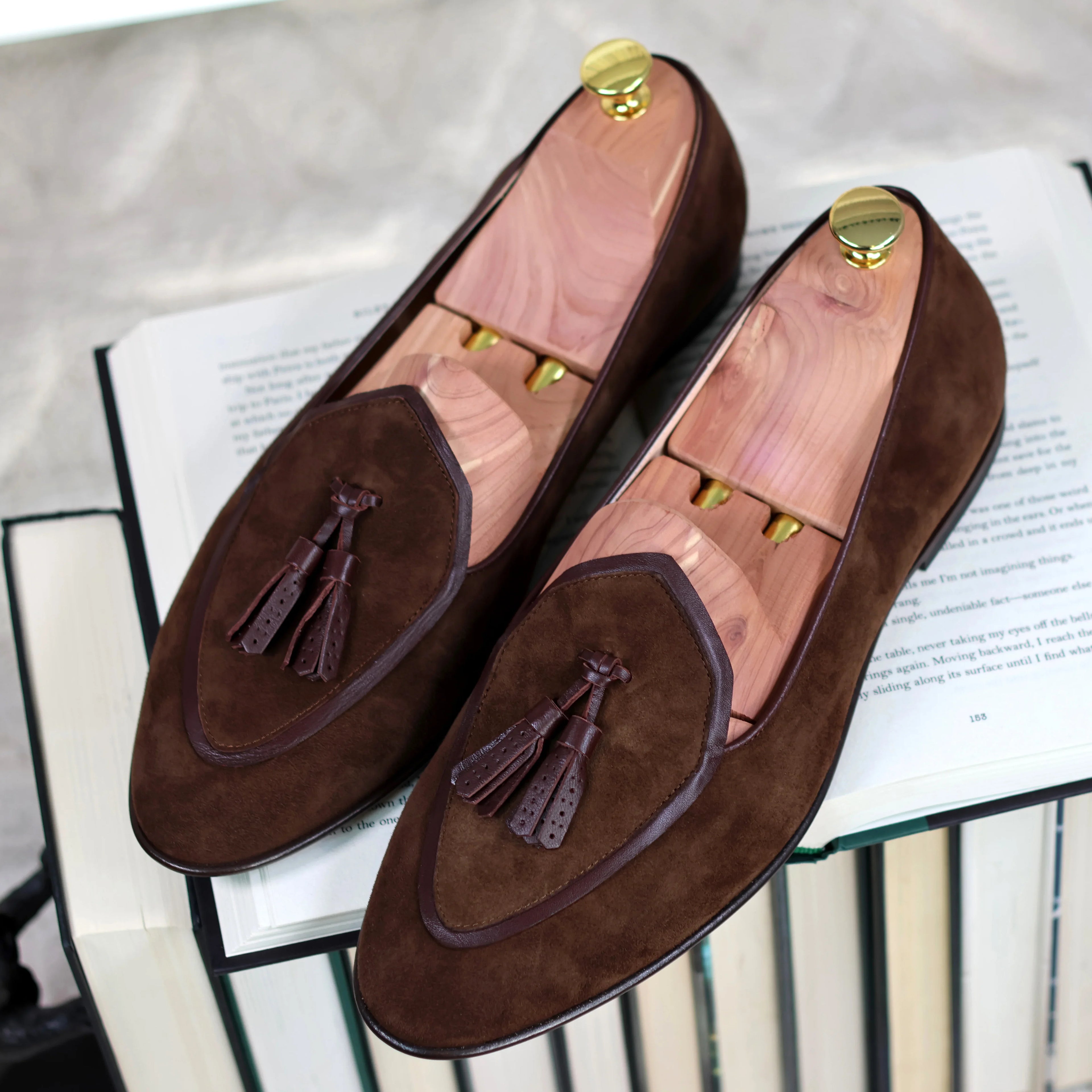 Brown suede JB Ander loafers with tassels on an open book
