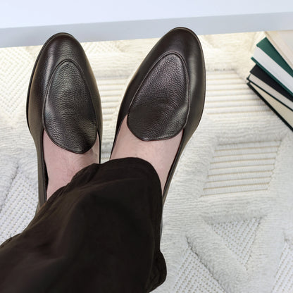 Person wearing JB Ander leather shoes on a textured surface with books in the background